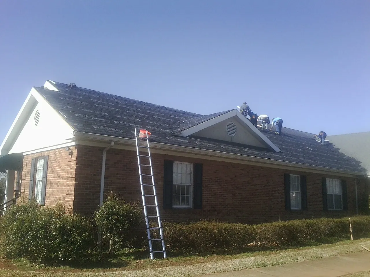 Crew tearing shingles off a brick ranch roof with a ladder set — Metal Roof Repair work by our crew in Odell