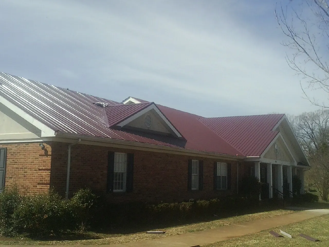 Red metal roof with gabled entries on a long brick building, from a Hail Damage Roof Repair job in Odell