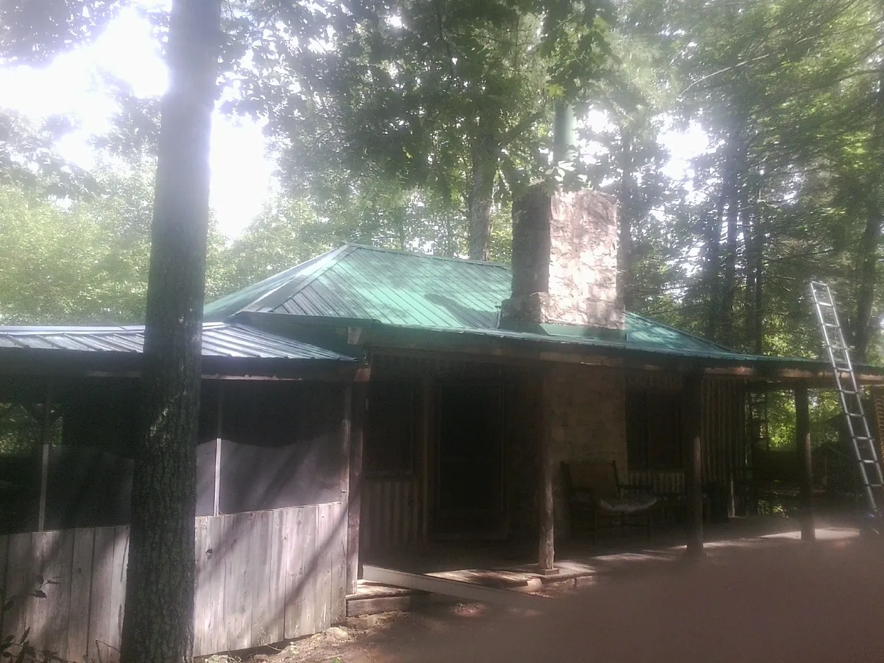 Green metal roof and stone chimney above a log cabin porch in Odell