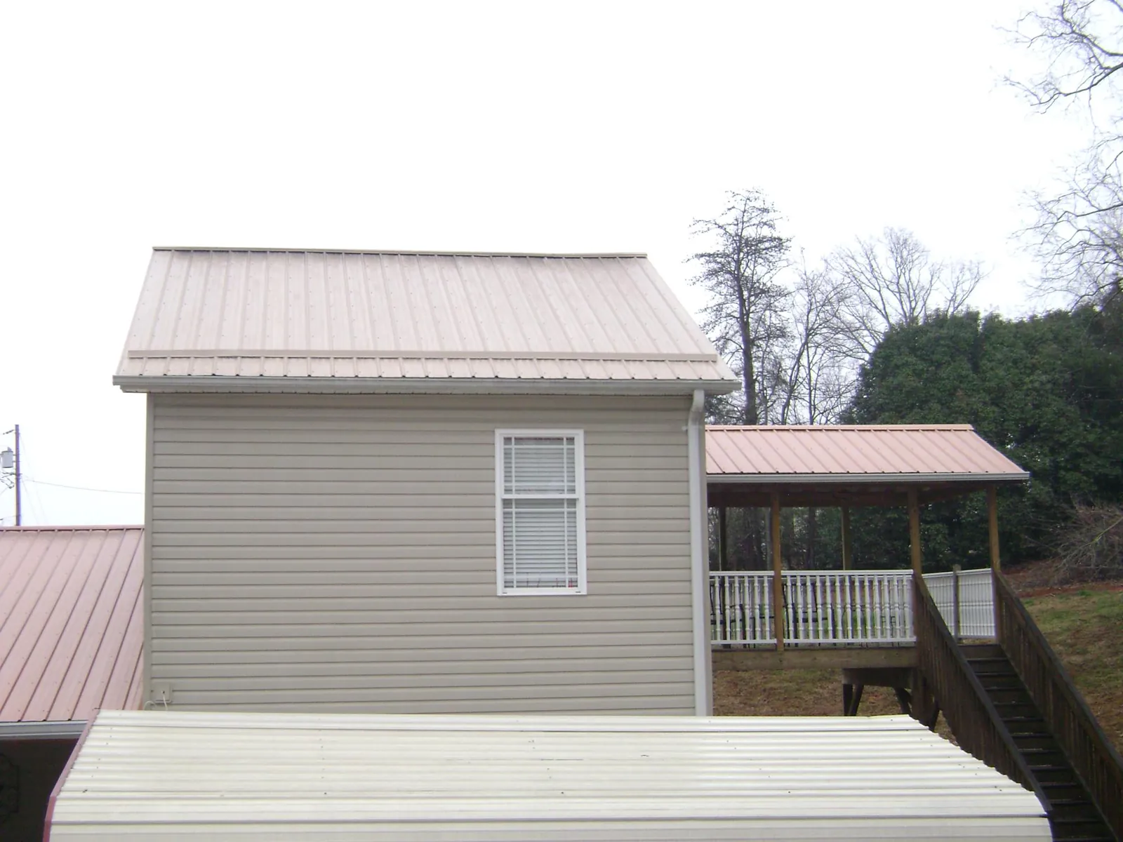 Tan metal roofs on a two story addition and attached porch, from a Roof Replacement job in Odell